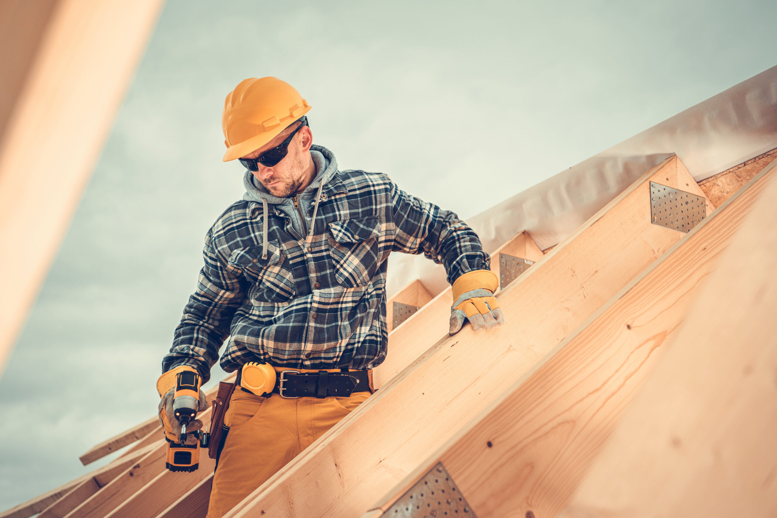 Wooden House Roof Skeleton Frame Assembly by Professional Construction Worker. Caucasian Contractor Wearing Yellow Hard Hat.