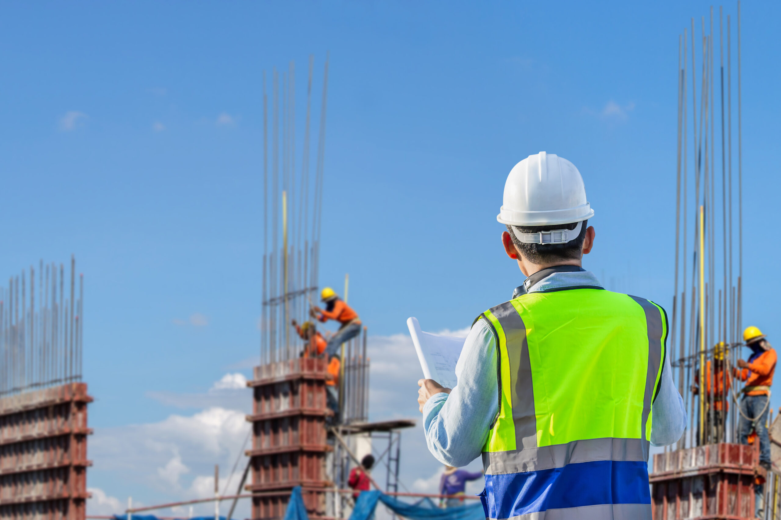 Engineer man with clipping path checking project at building site, blurred workers team at construction site background